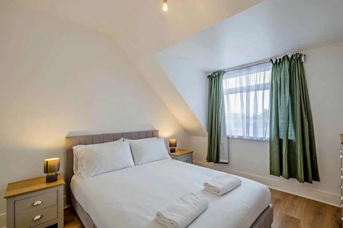 Un dormitorio con una cama bien tendida y cortinas verdes junto a la ventana.