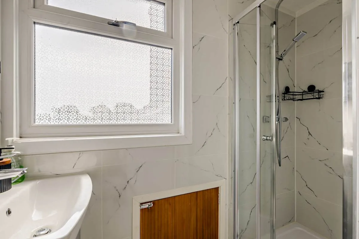 Un baño con ducha de vidrio, lavabo y ventana esmerilada.