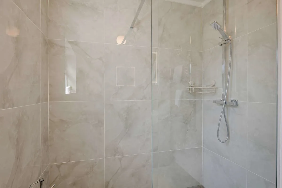 Una zona de ducha con azulejos, una alcachofa de pared y un panel de vidrio.