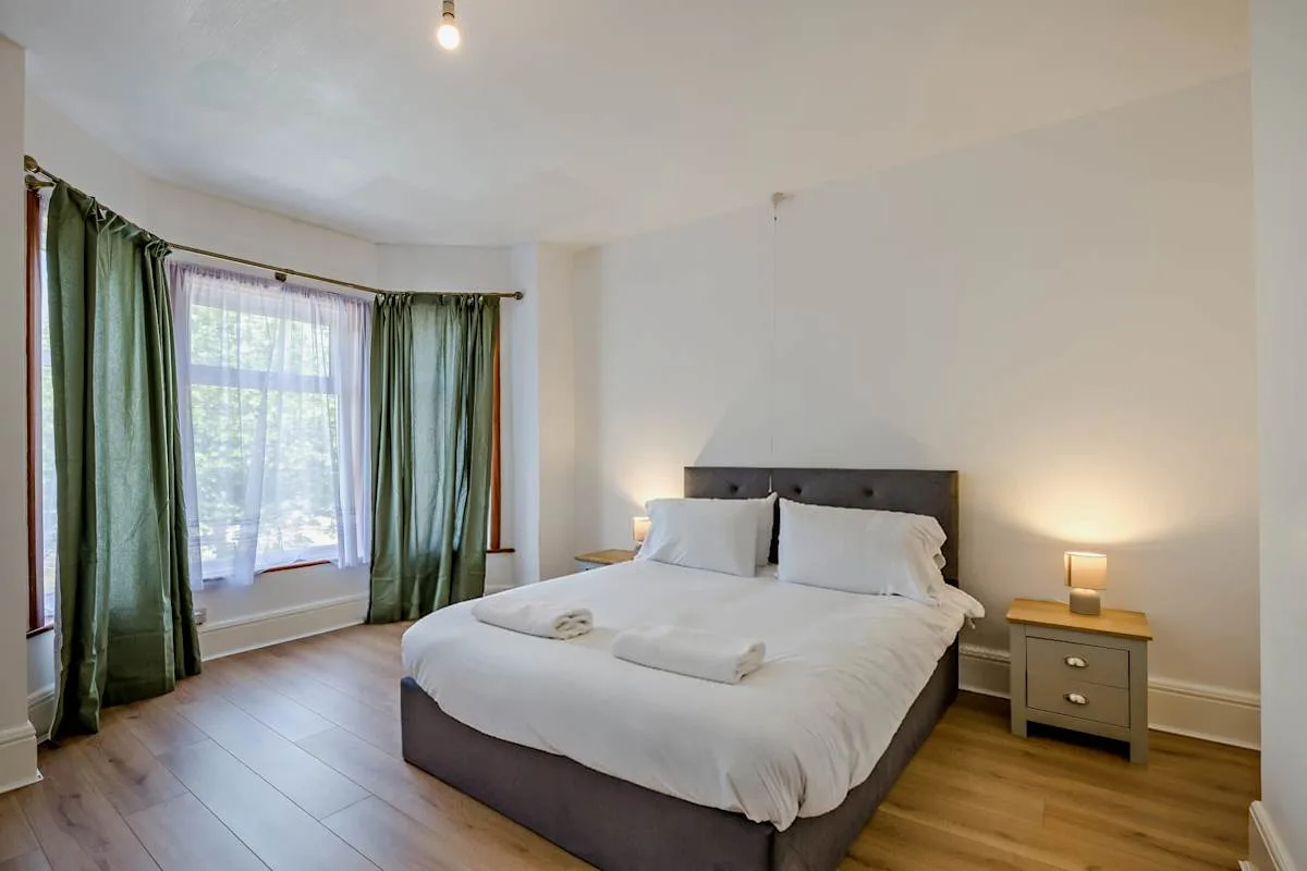 Un dormitorio con una cama doble, cortinas verdes y una mesita de noche.