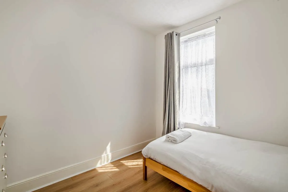Un dormitorio luminoso con una cama junto a una ventana alta con cortinas.