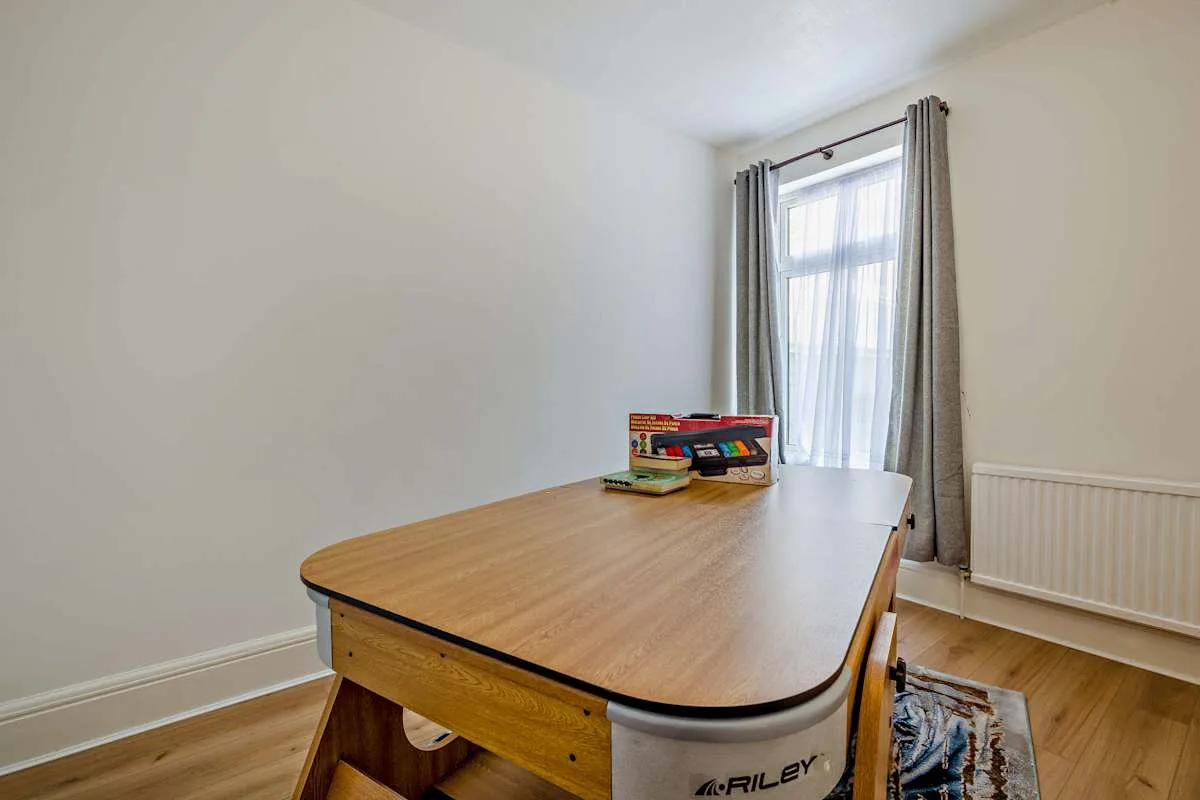 Una habitación luminosa con un escritorio grande de madera junto a una ventana con cortinas.