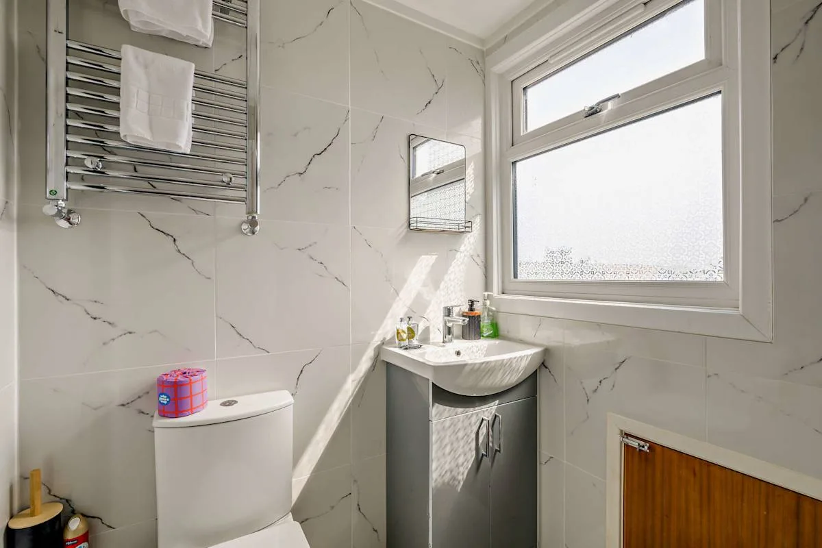 Un baño alicatado con lavabo, inodoro y una ventana luminosa.