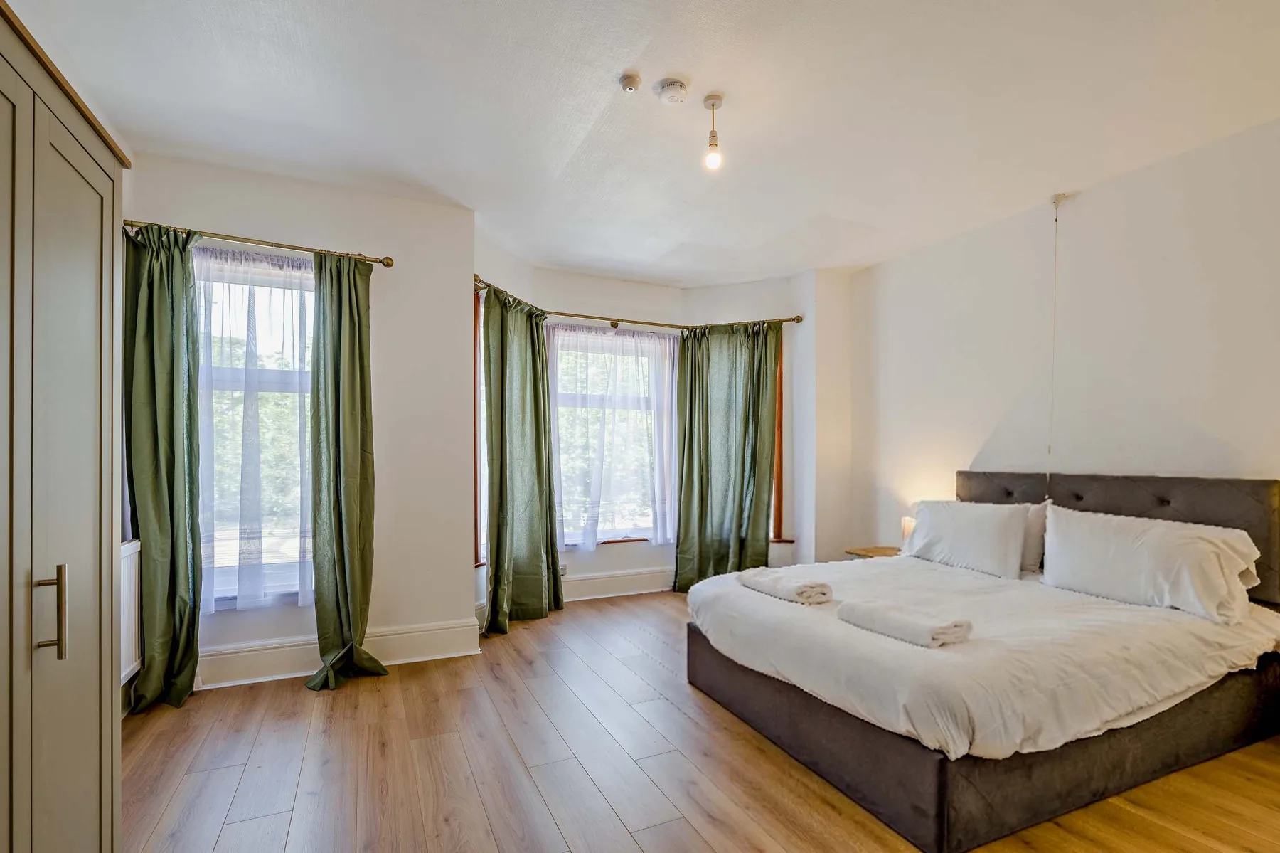 Un dormitorio con una cama grande y ventanas altas enmarcadas por cortinas verdes.