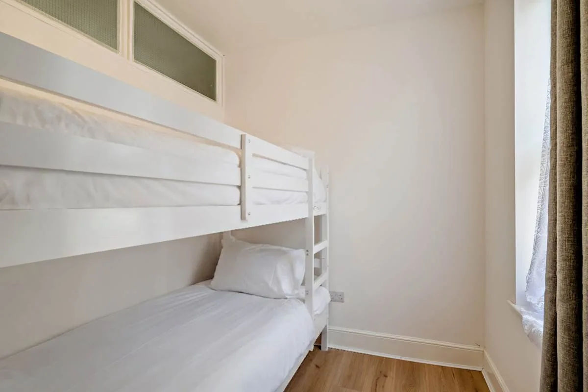 Dormitorio luminoso con una litera blanca junto a una ventana con cortinas.