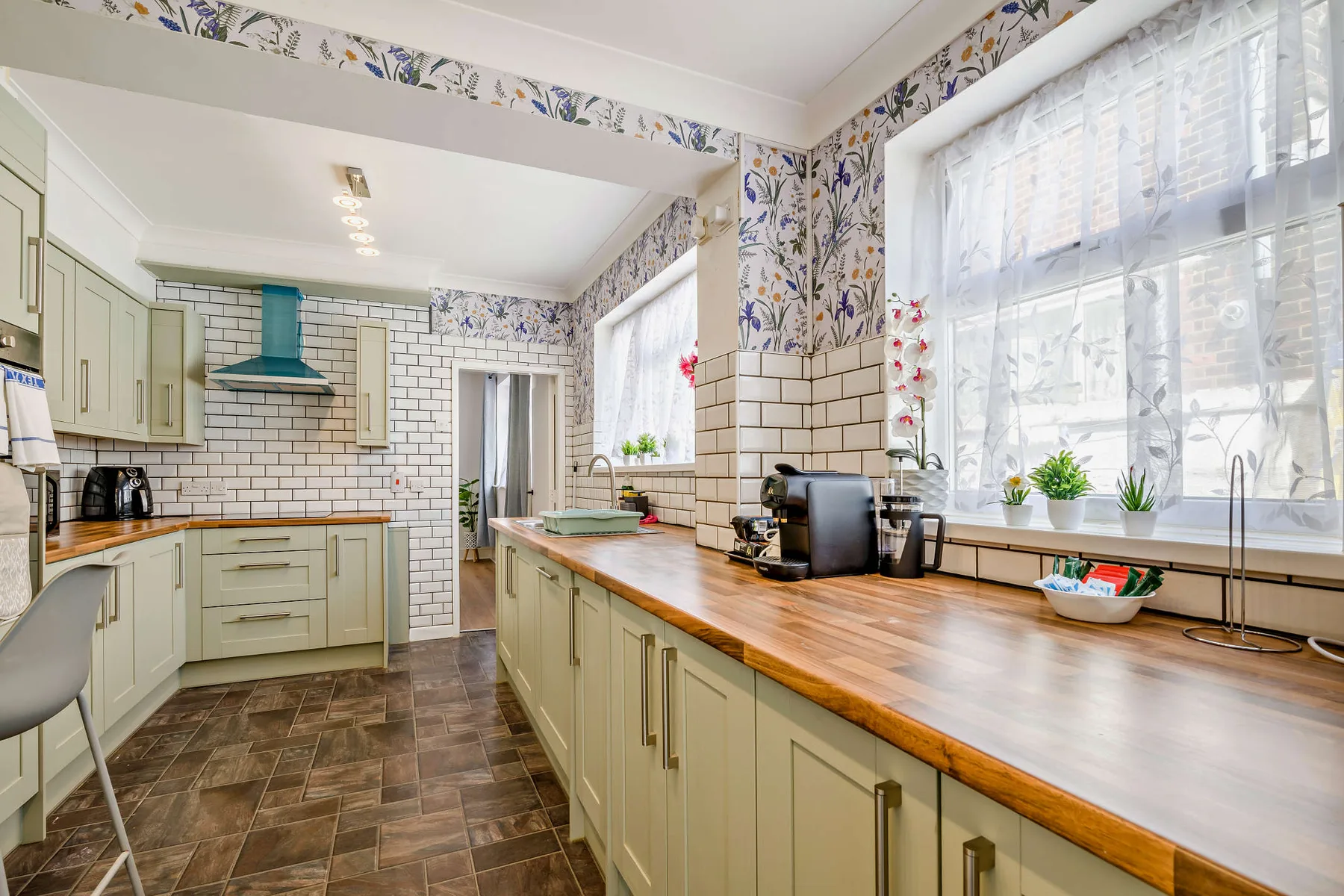Una cocina luminosa con armarios claros, encimeras de madera y ventanas grandes.