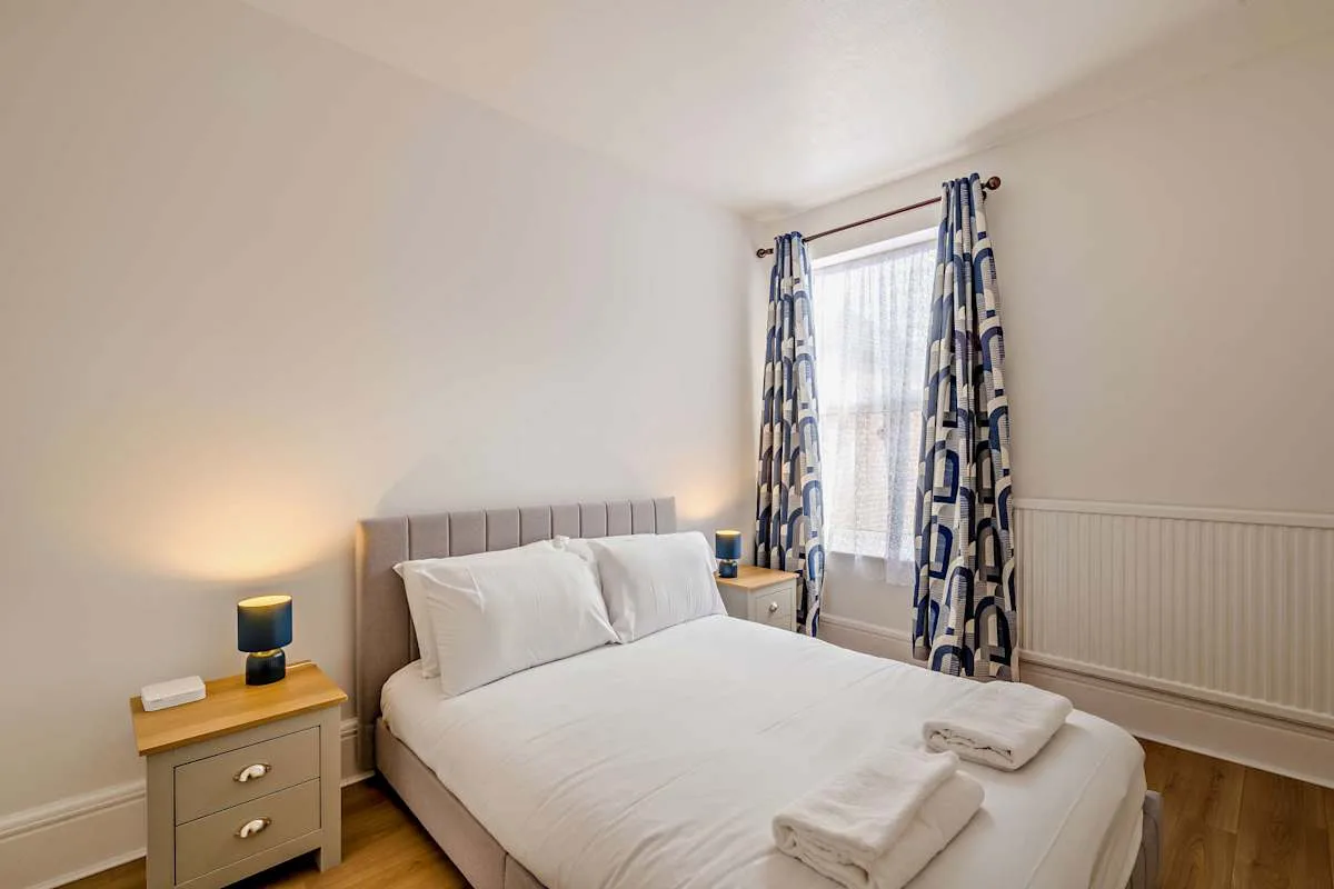 Un dormitorio luminoso con una cama bien hecha y cortinas estampadas.