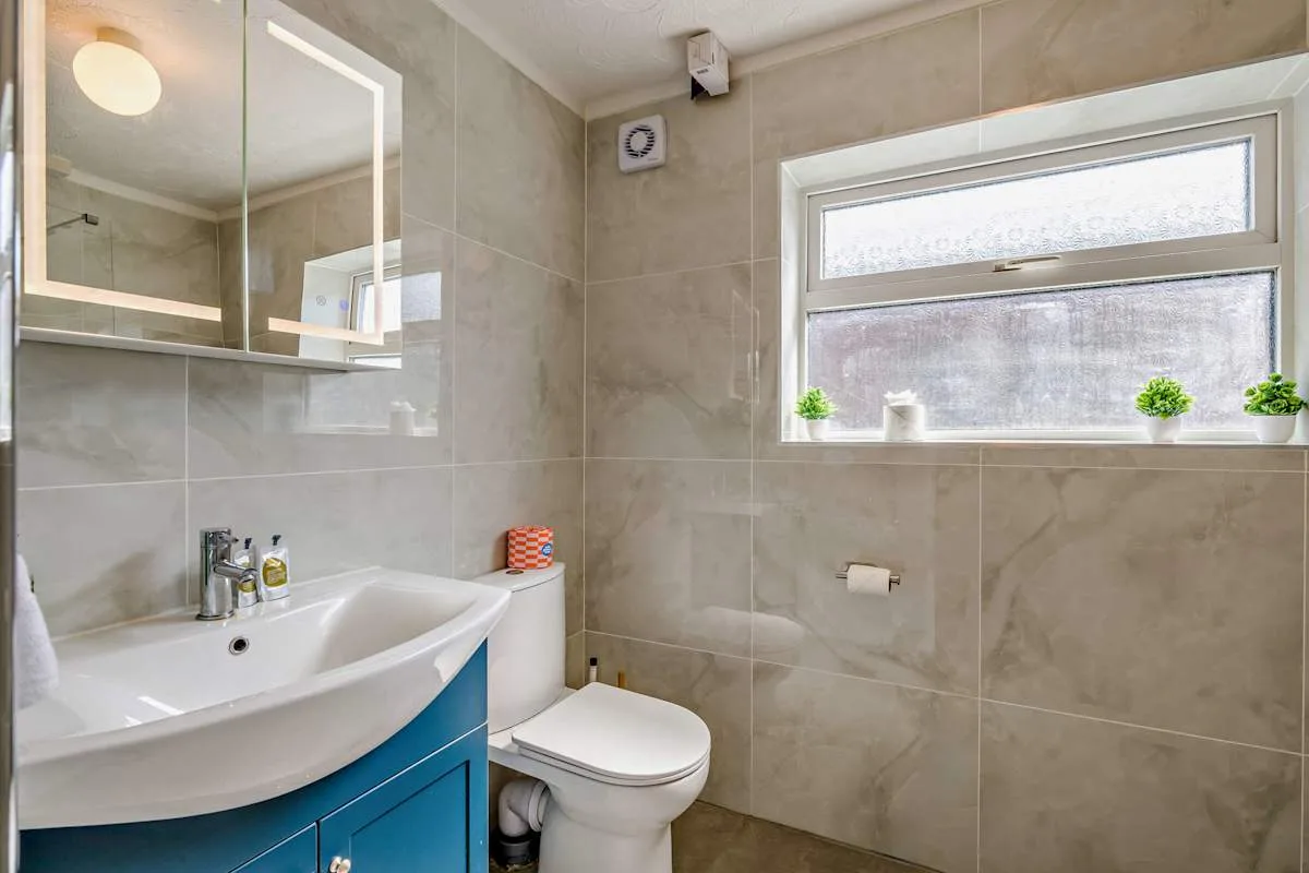 Un baño con azulejos, lavabo, inodoro y ventana.