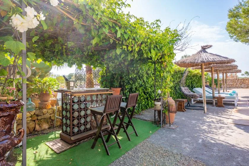 Una zona de bar y asientos a la sombra junto a una terraza soleada con piscina.