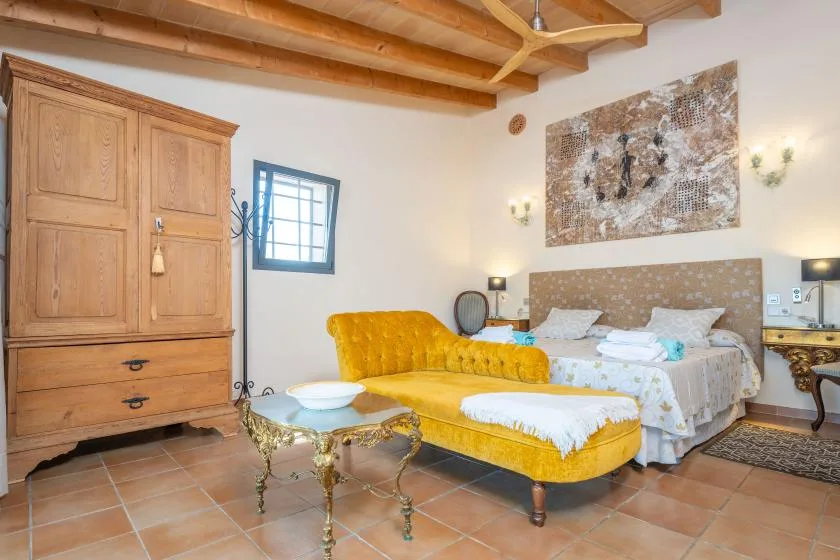 Un dormitorio con una cama y asientos amarillos bajo vigas de madera a la vista.
