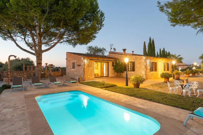 Una piscina y asientos al aire libre junto a una casa de piedra al anochecer.