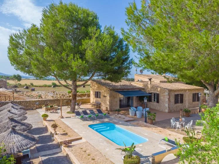 Una casa de piedra junto a una piscina, con árboles y asientos al aire libre.