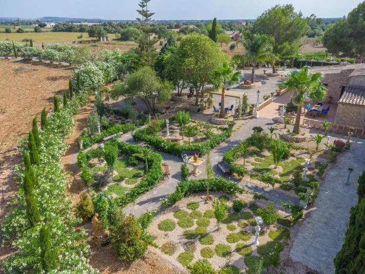 Vista aérea de jardines ajardinados con senderos sinuosos, árboles y campos alrededor.