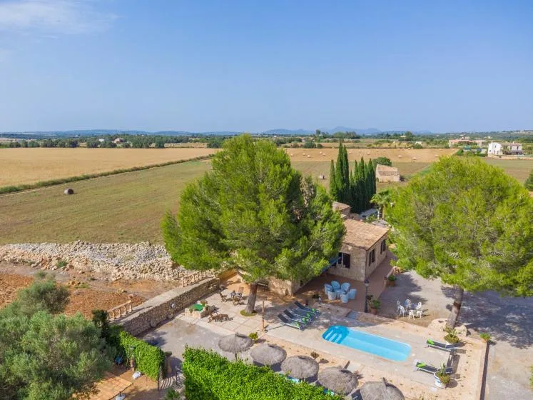 Una casa rural y una piscina están entre árboles junto a campos abiertos.