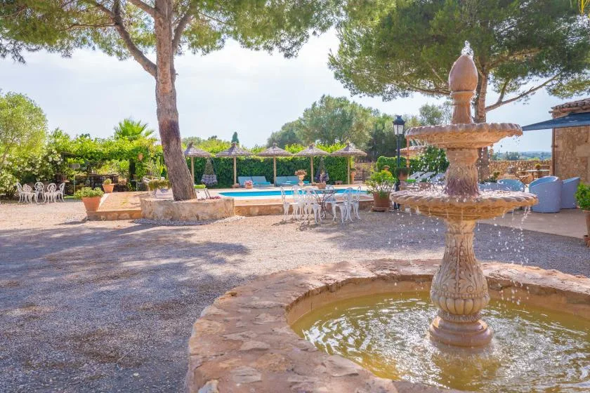 Un patio exterior cuenta con una fuente de piedra, asientos a la sombra y una piscina.