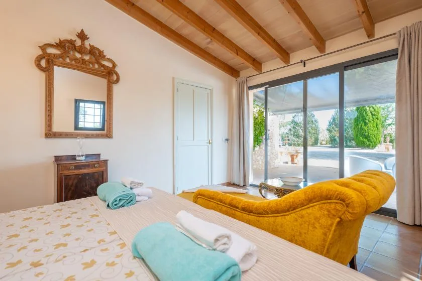 Un dormitorio con cama, espejo decorativo y una luminosa zona de estar junto a puertas corredizas de vidrio.