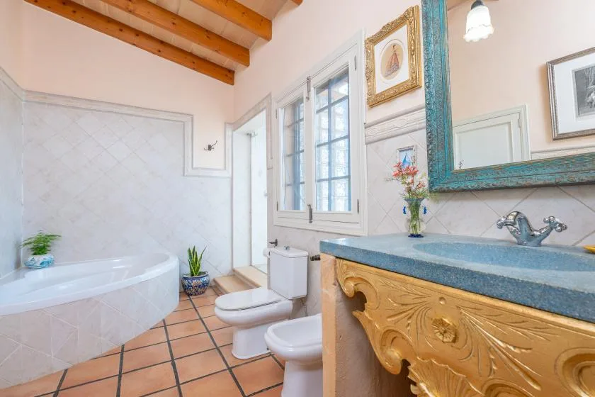 Un baño luminoso con bañera, inodoro y un lavabo ornamentado bajo un espejo grande.