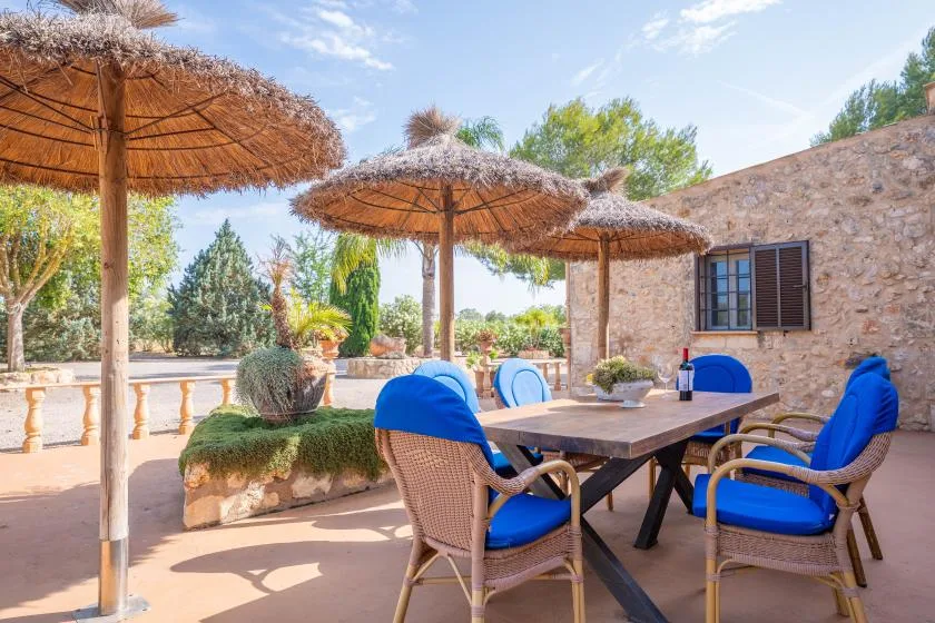 Comedor al aire libre con una mesa y asientos con cojines azules bajo sombrillas de paja.