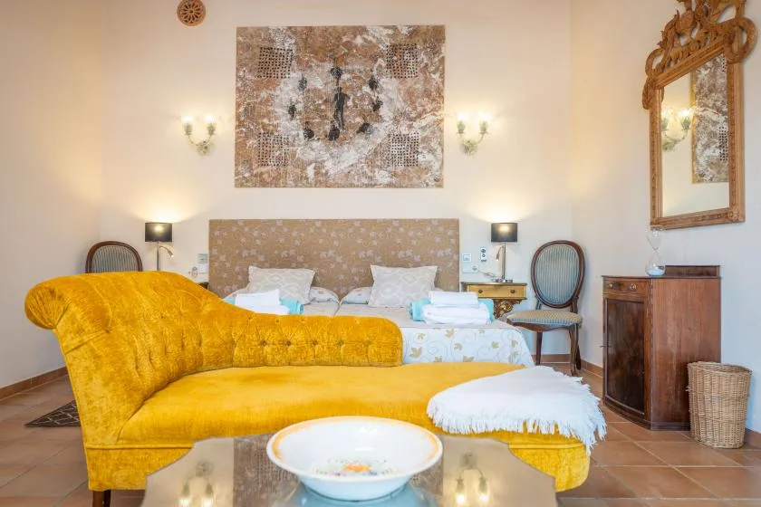Un dormitorio con una cama, asientos mostaza y arte en la pared.