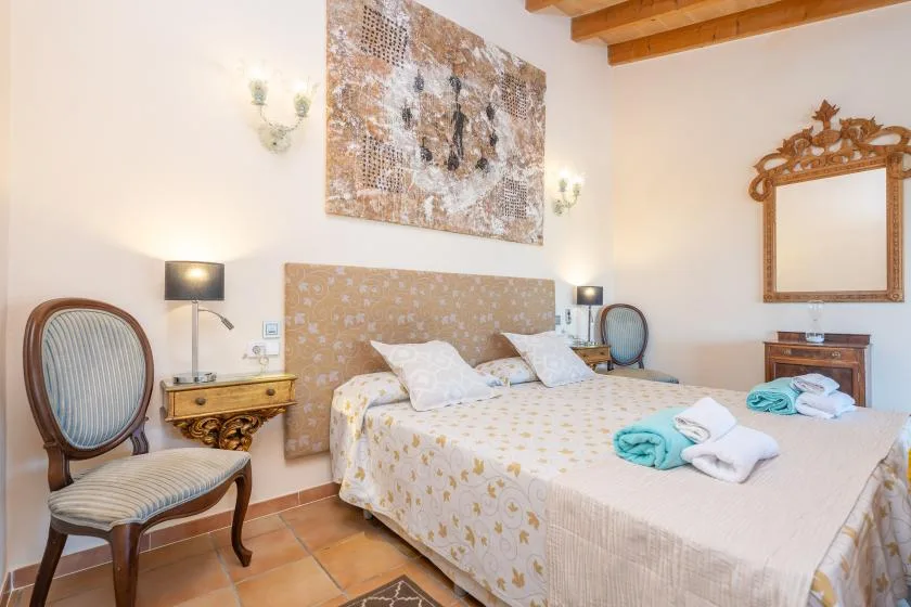 Un dormitorio con una cama, sillas tapizadas y un espejo enmarcado.