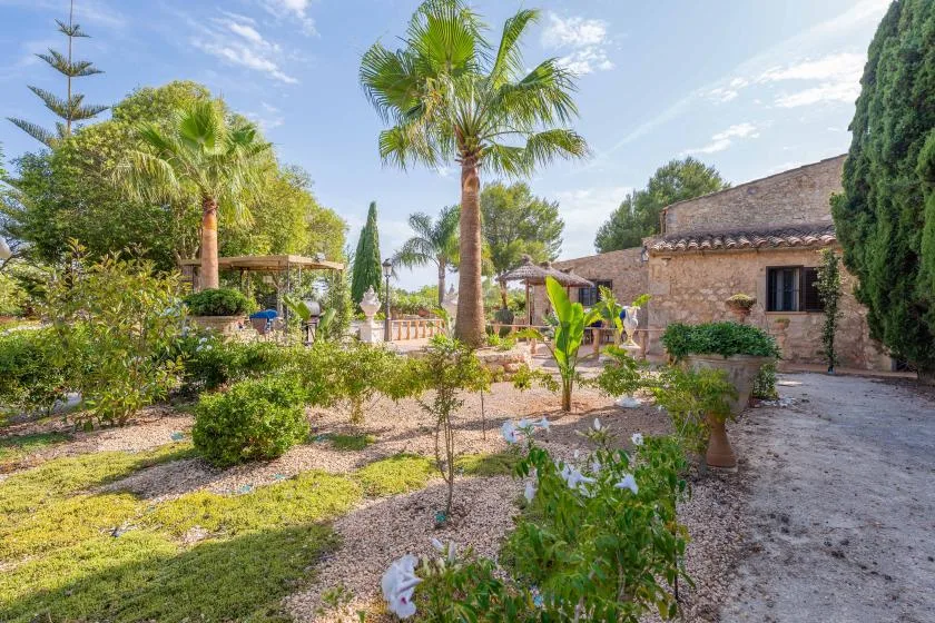 Un jardín con palmeras, arbustos y un edificio de piedra.