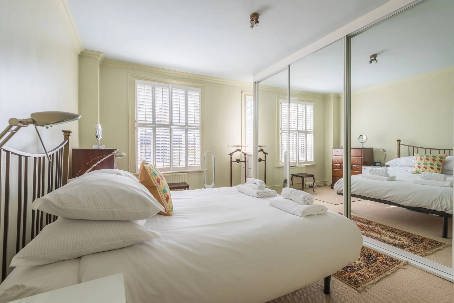 A bright bedroom with a neatly made bed and mirrored wardrobe doors.