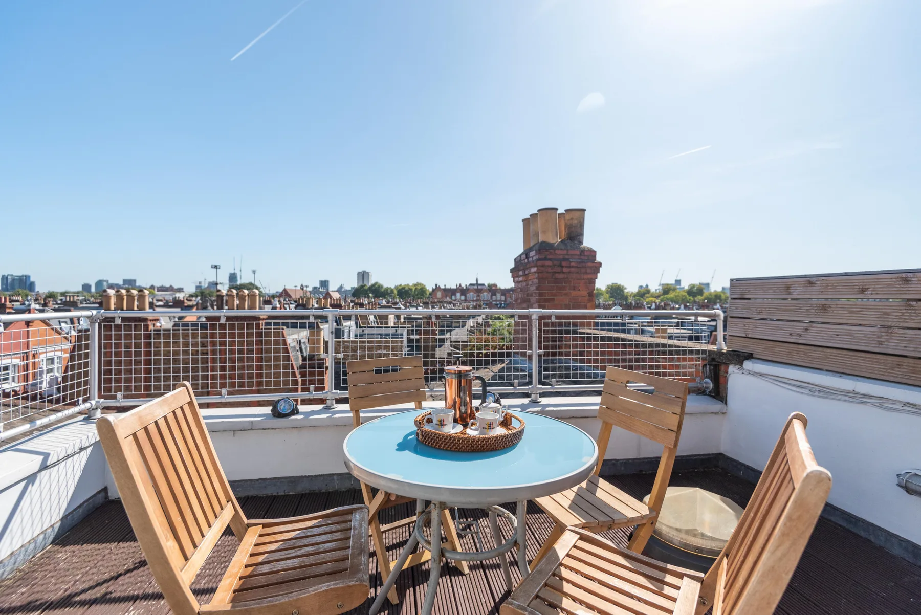 A rooftop terrace has wooden seating around a small table overlooking the city.