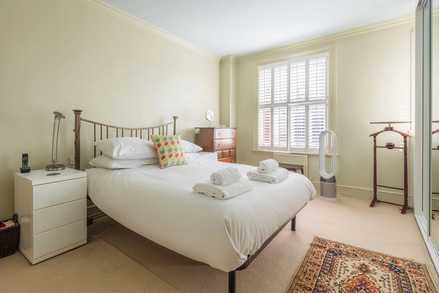 A bedroom with a neatly made bed and a large shuttered window.