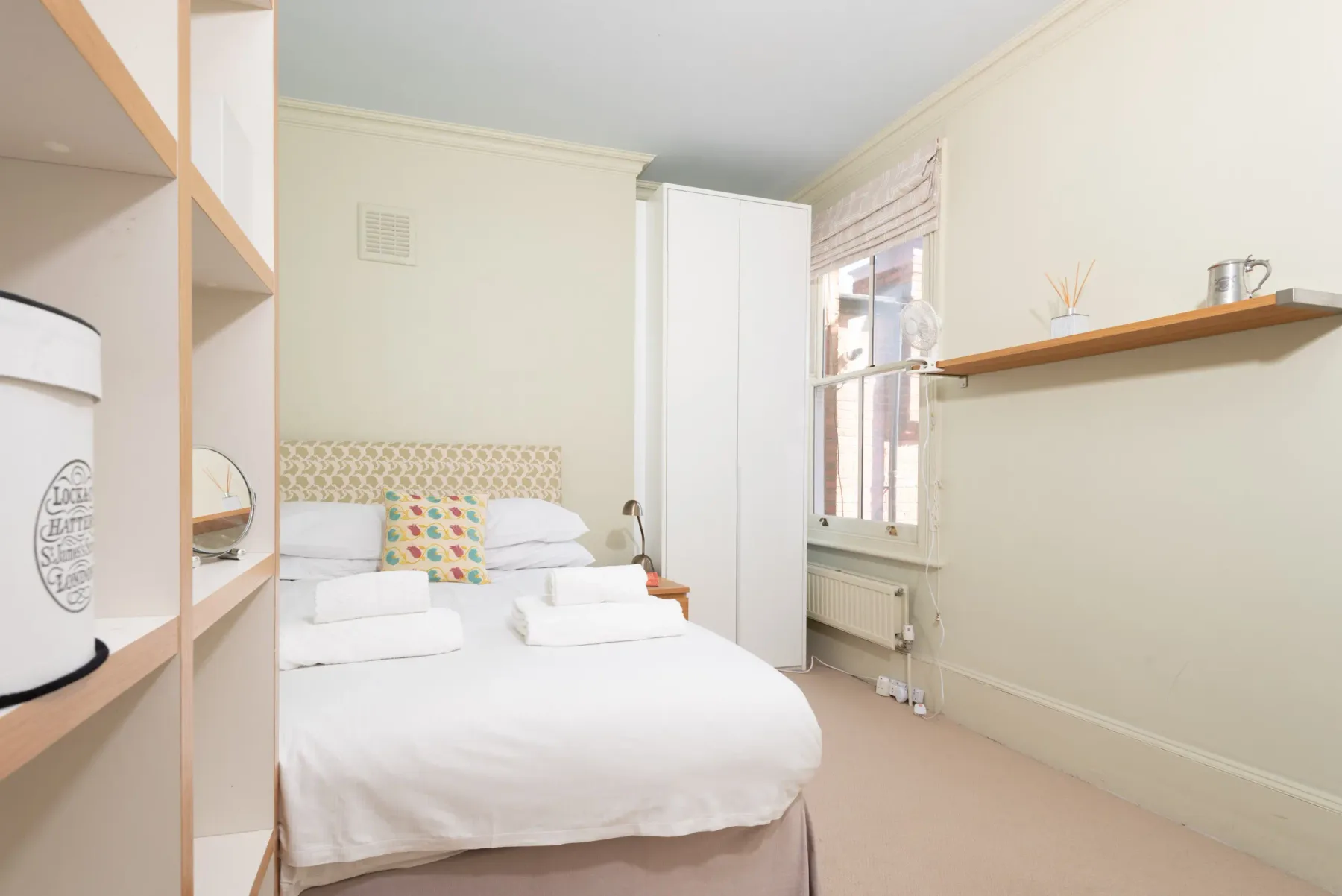 A bright bedroom with a neatly made bed beside a window.