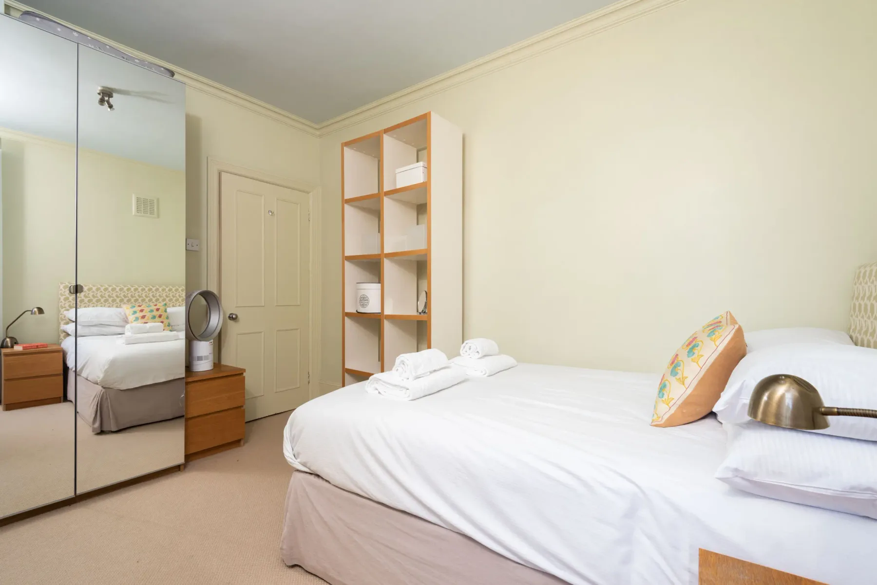 A bright bedroom with a neatly made bed and mirrored wardrobe.