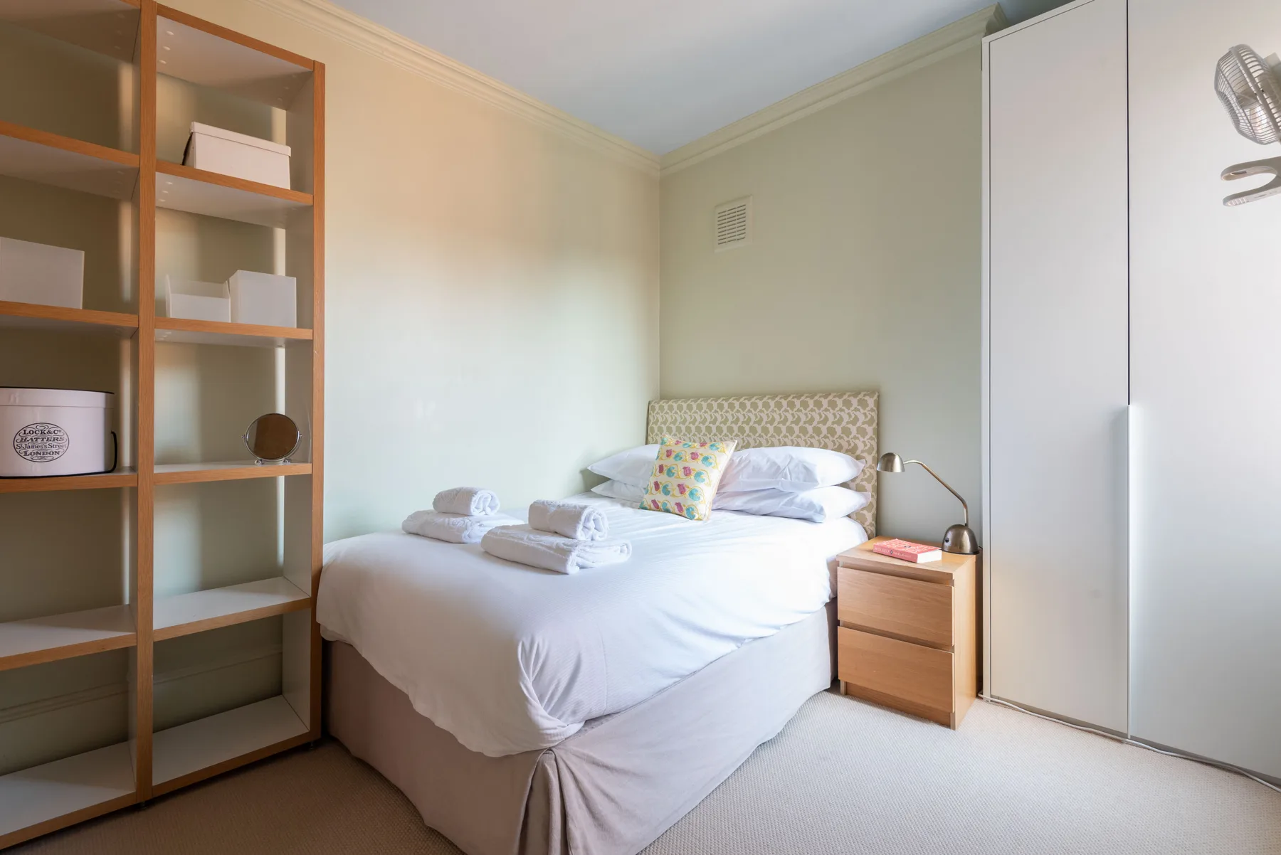 A bedroom with a neatly made bed and open shelving along the wall.