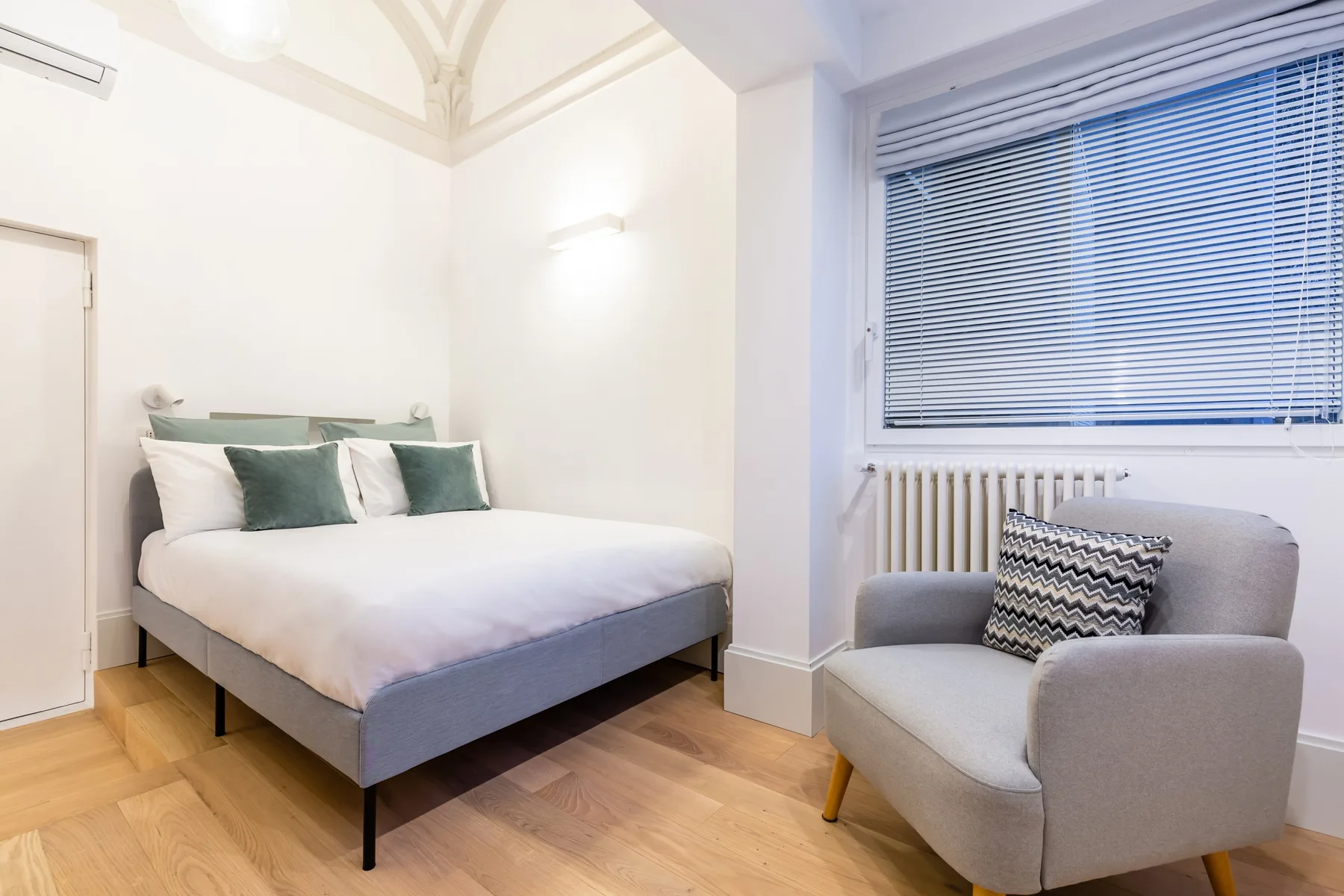 Un dormitorio con una cama y un sillón tapizado junto a la ventana.