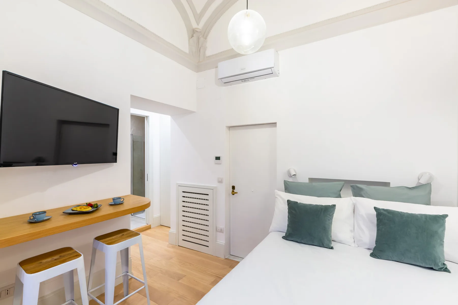 Dormitorio con cama, televisor en la pared y un pequeño escritorio.