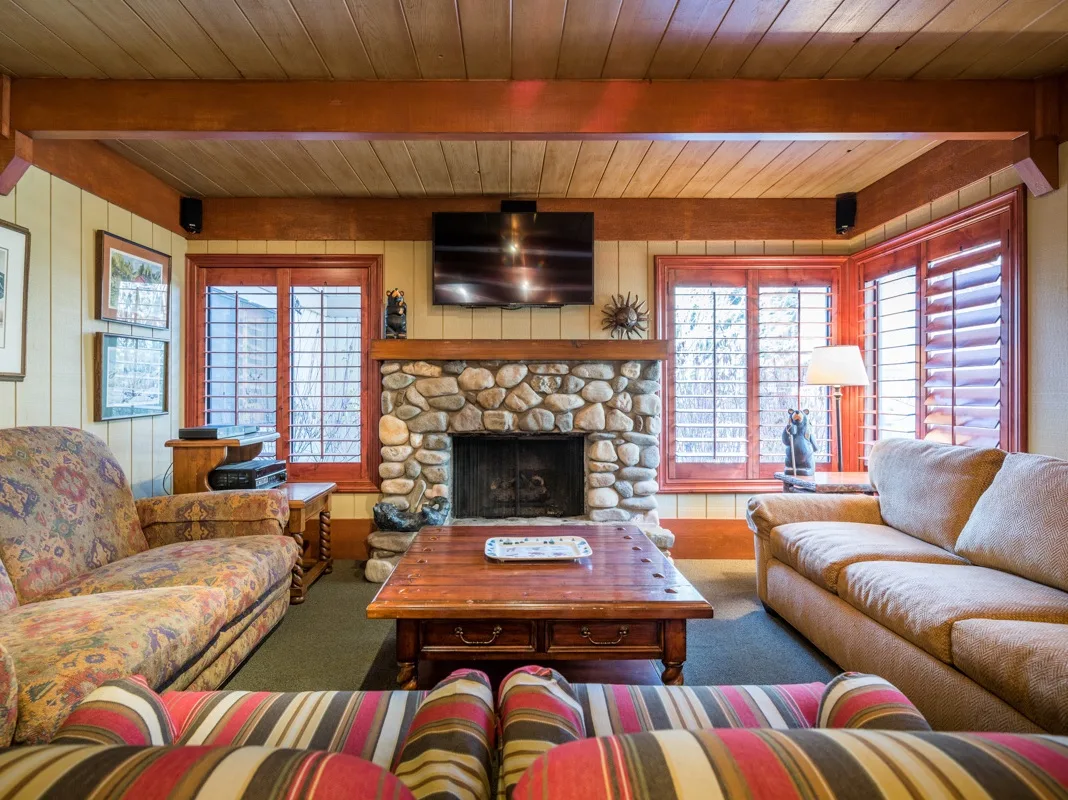 Una sala con paneles de madera, chimenea de piedra, televisor y asientos.