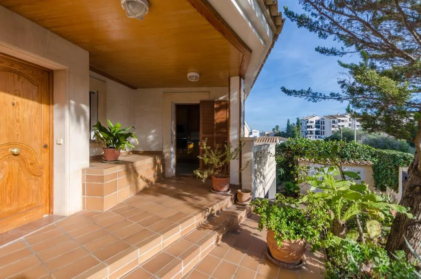 A tiled outdoor terrace with a wooden door, potted plants, and garden views.