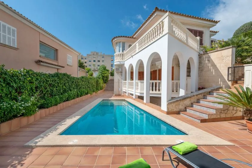 A swimming pool beside a white building with arched columns and a staircase.