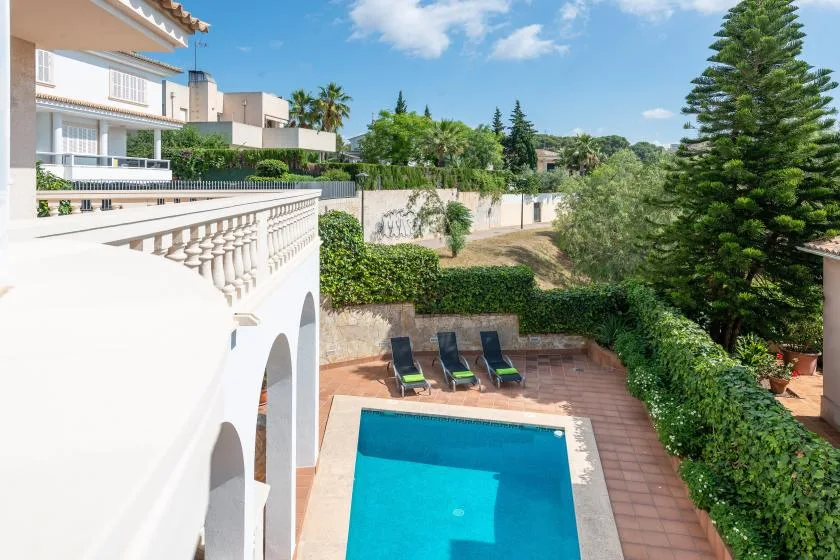 An outdoor swimming pool sits beside a tiled terrace and green hedges.