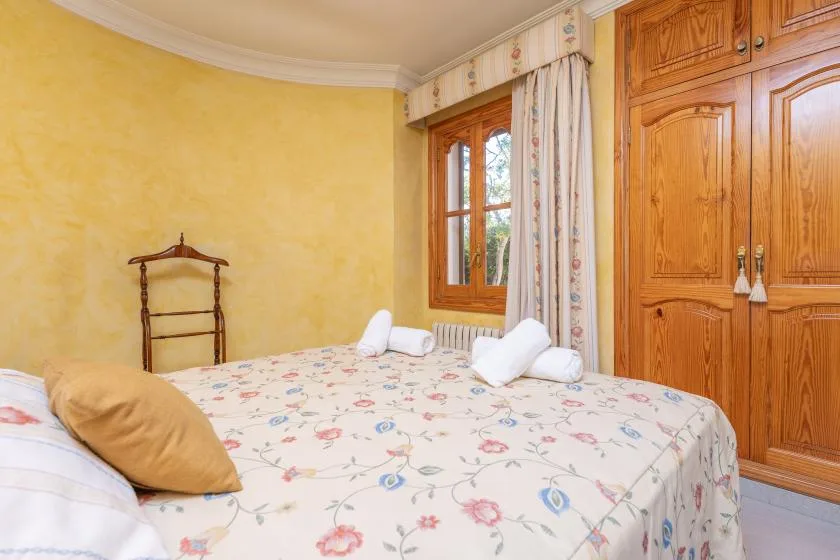 A bedroom with a floral bedspread, wooden wardrobe, and curtained window.