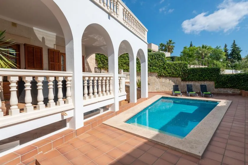 A swimming pool beside a white arched terrace on a sunny day.