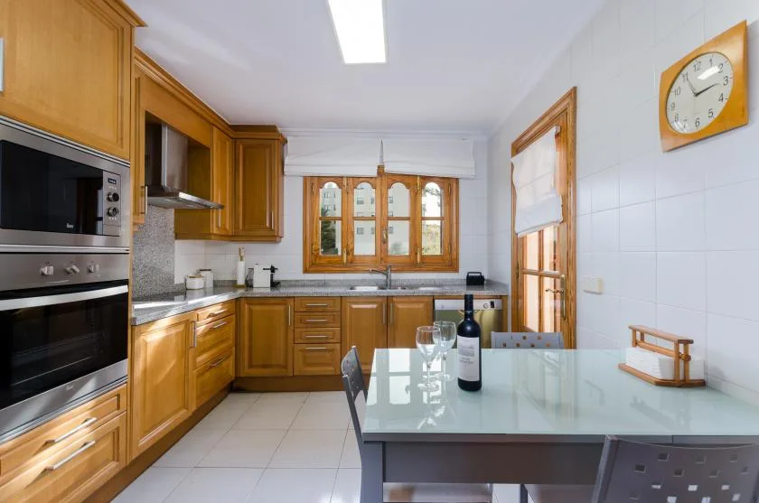A bright kitchen with wooden cabinets and a glass-topped dining table.