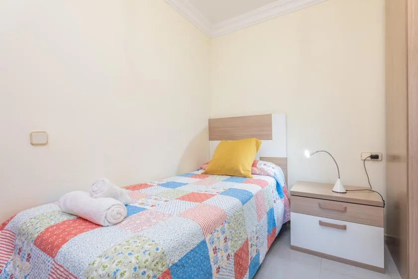 A bedroom with a single bed covered by a colorful quilt and a bedside table.