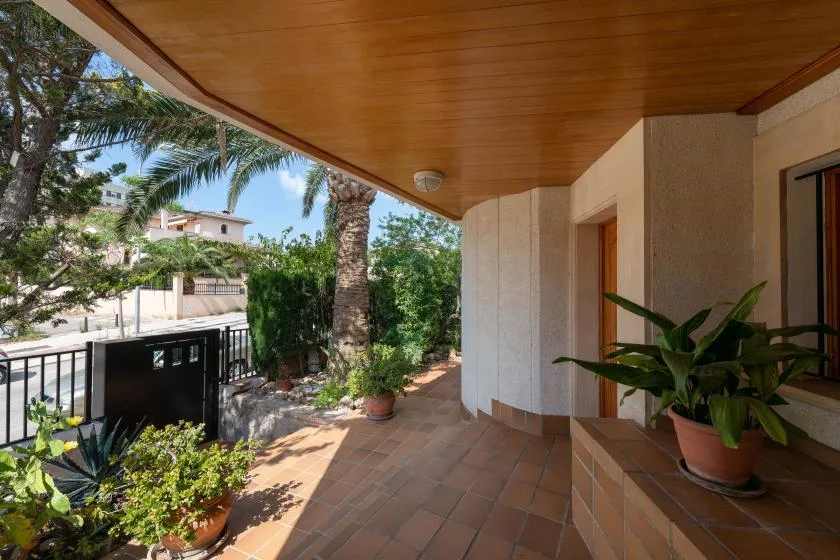 A covered outdoor patio with tiled flooring, potted plants, and a garden view.