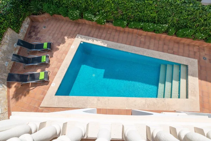 A swimming pool sits in a tiled patio beside several lounge chairs.