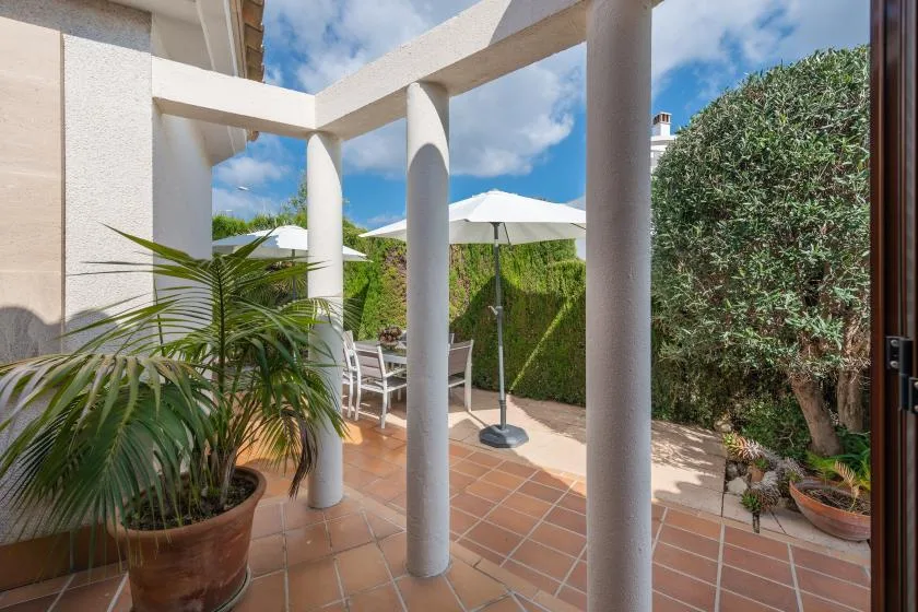 A covered patio with terracotta-colored tiles, outdoor seating, and a white umbrella.