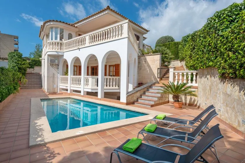 A white villa with an outdoor swimming pool and lounge chairs.