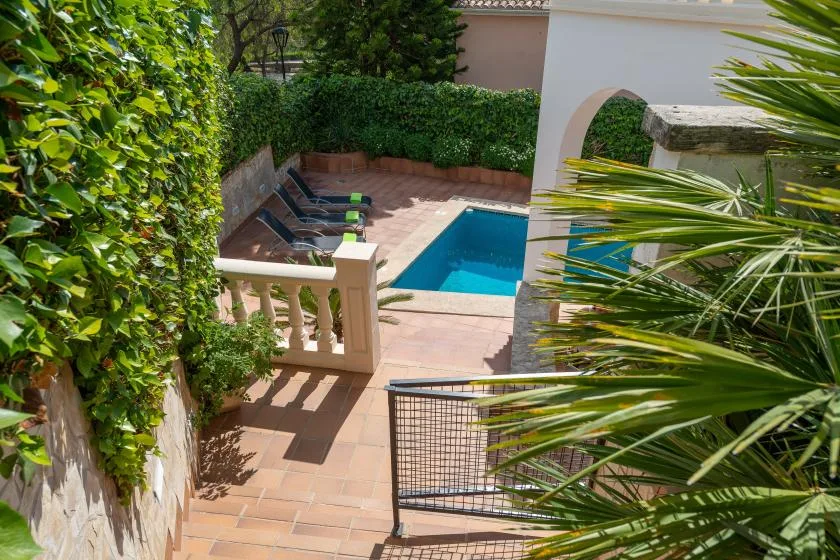 A tiled outdoor patio overlooks a small rectangular swimming pool surrounded by greenery.