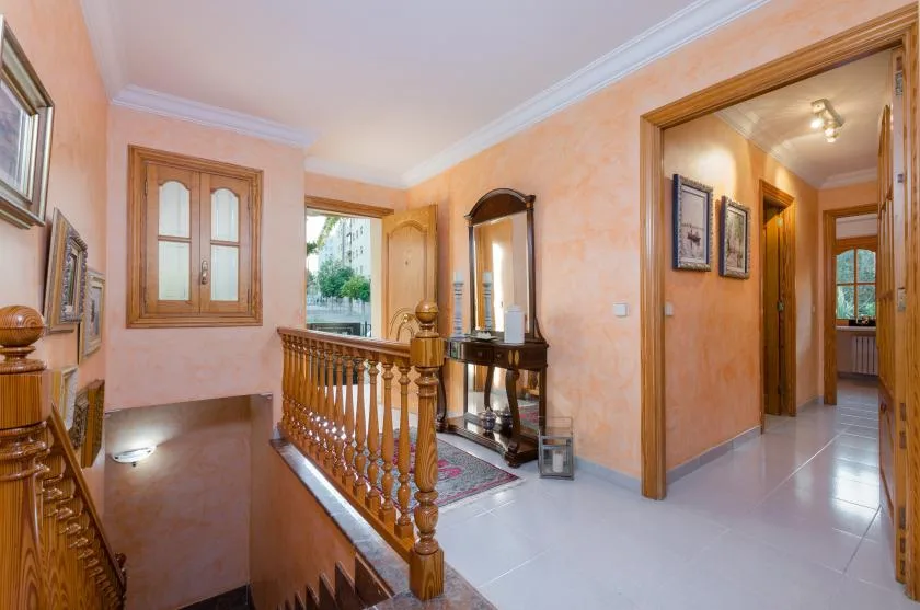 A peach-colored hallway with a wooden stair railing, a window, and an open doorway.