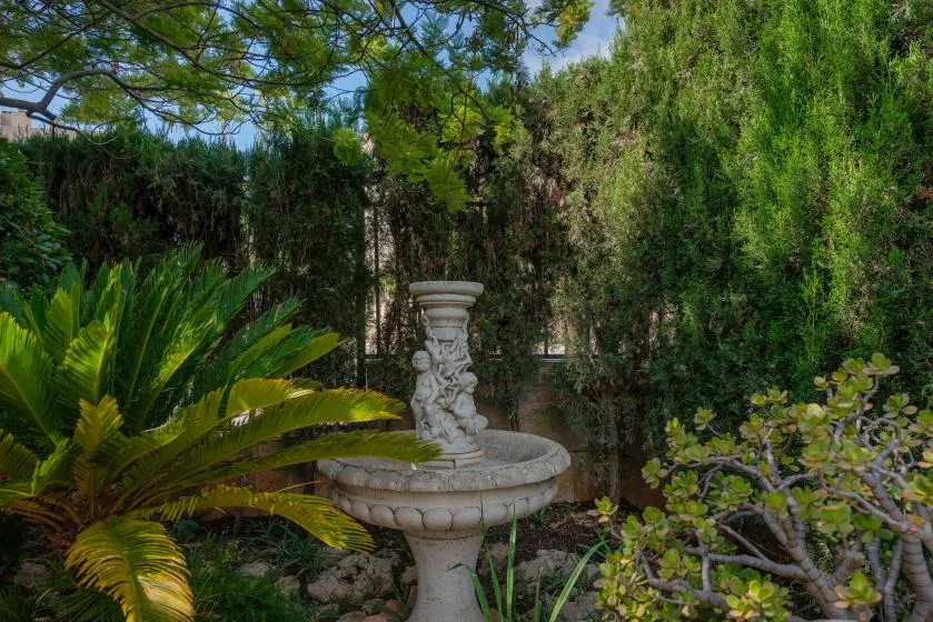 A stone fountain stands among dense greenery in a garden.