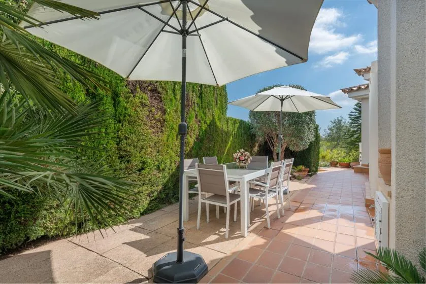 An outdoor dining patio with a table and umbrellas beside a garden.