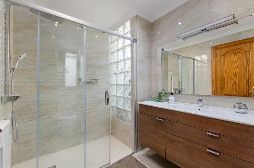 A bathroom with a glass shower and a wood vanity beneath a wide mirror.